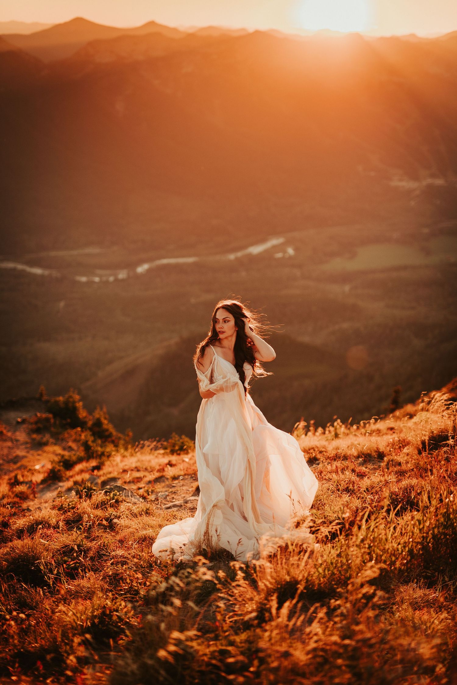 A flowing white dress catches the golden light as bride twirls on a mountain summit at sunset.