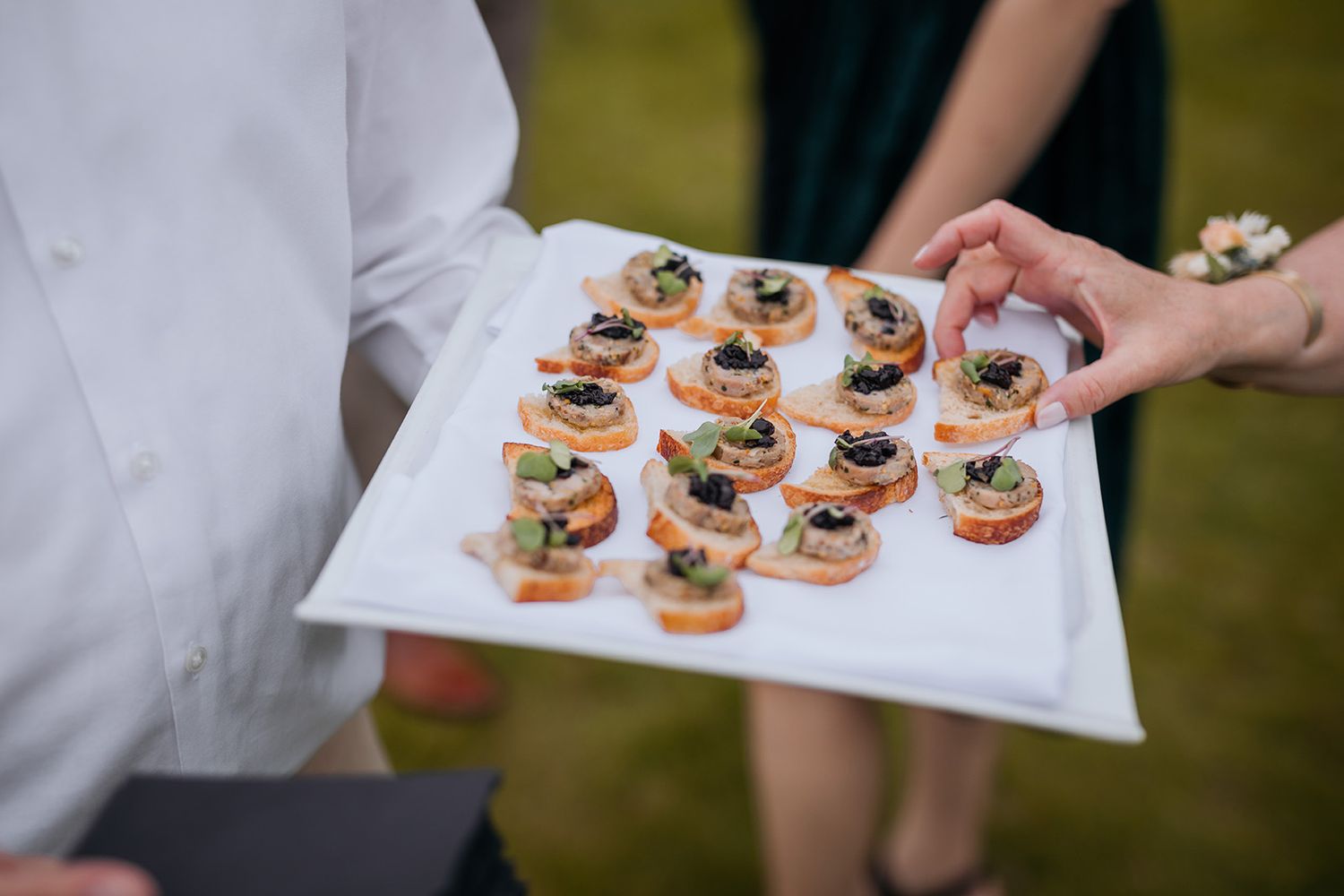 Servers carry white platters of elegant canapé appetizers at an upscale catering event.