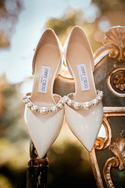Elegant white bridal shoes with pearl embellishments displayed against a soft blurred background.
