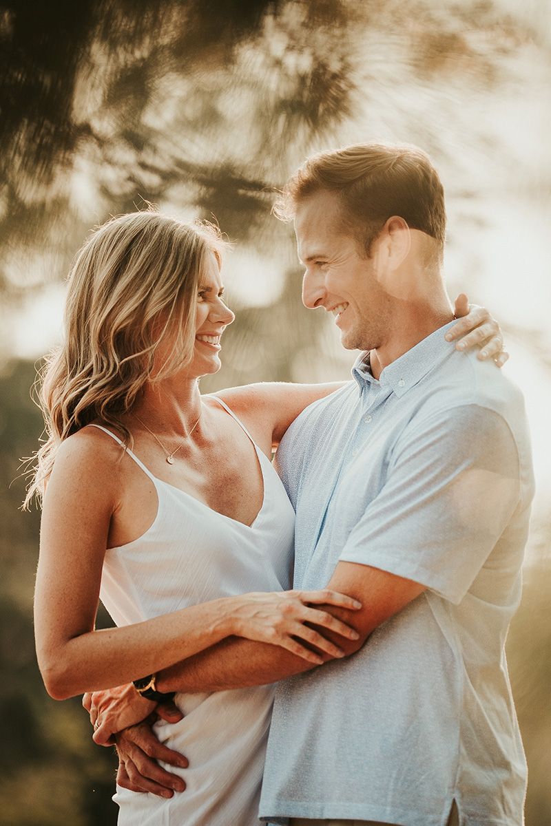 A romantic couple embraces in warm golden sunlight during an outdoor portrait session. Lens bokeh provides an ethereal vibe.