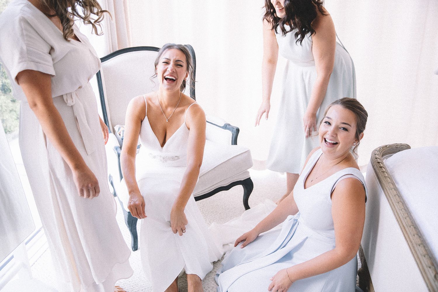A group of women in white dresses share a joyful moment while getting ready for a wedding celebration.