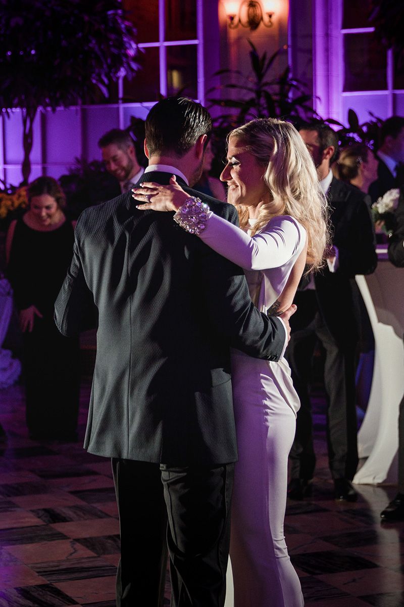 Bride and groom dance together at an elegant reception with purple lighting casting a romantic glow on the dance floor.