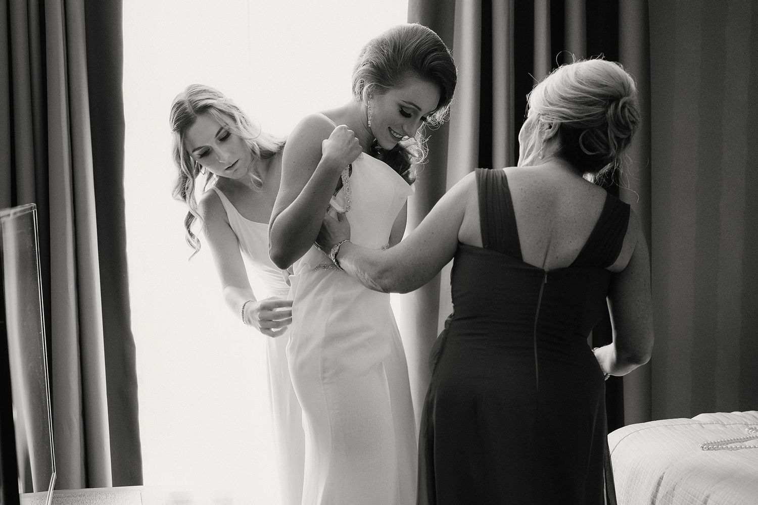 Black and white photo sequence showing bride getting dressed and helped into wedding gown during preparation.