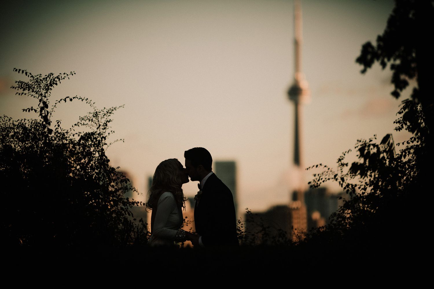 Silhouetted couple sharing an intimate moment at sunset with Toronto's CN Tower in the background.