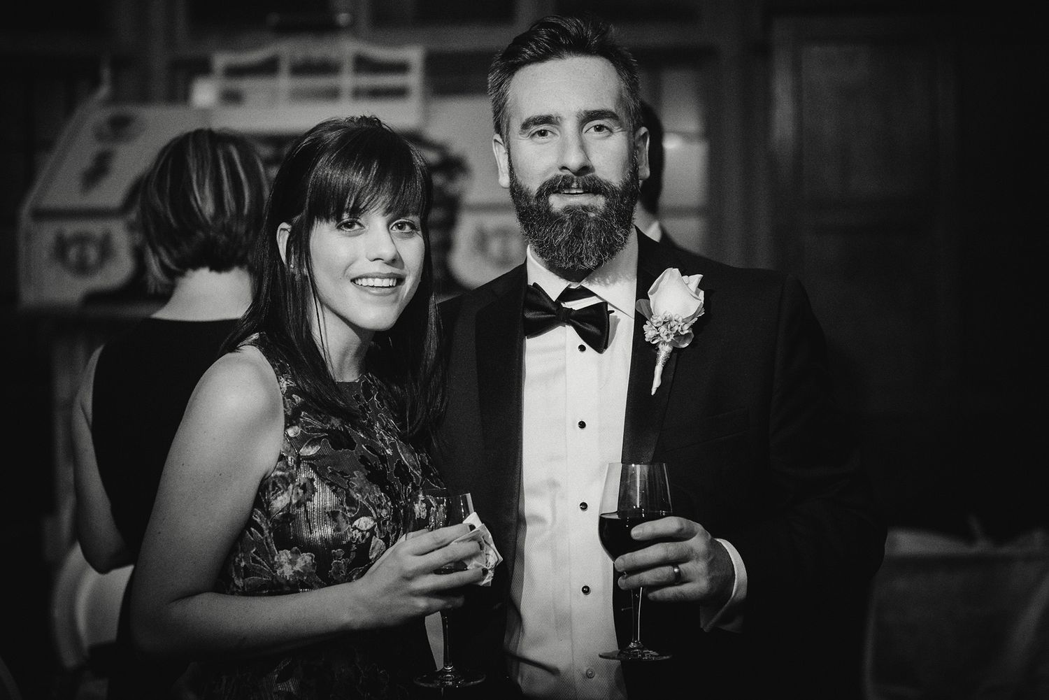 Black and white photo of a couple in formal attire at an elegant party holding drinks and smiling.