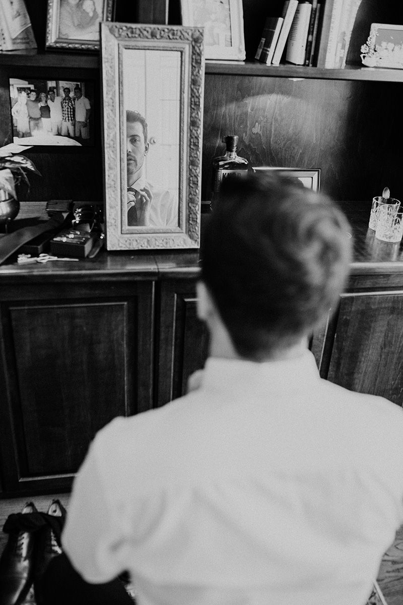 Vintage black and white photograph showing a man in white shirt looking at himself in a narrow mirror.