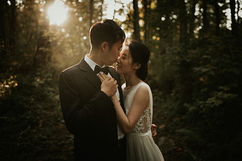A romantic couple in wedding attire embrace during golden hour in a moody forest setting.
