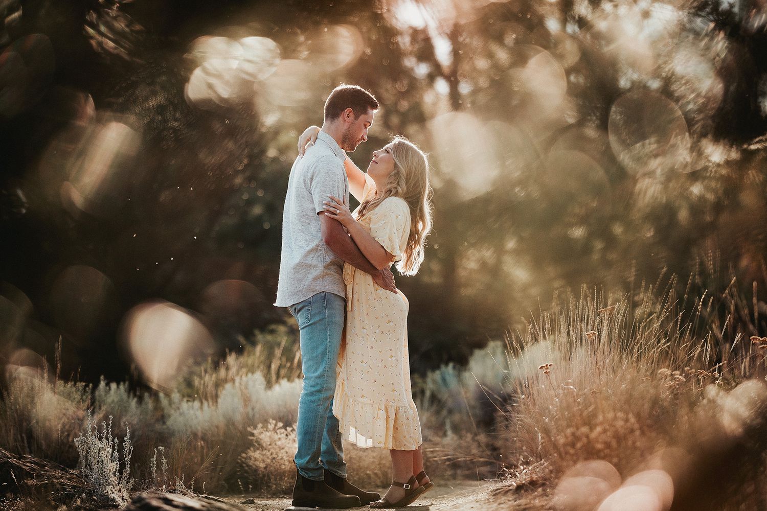 A romantic couple embraces in a sun-drenched field during a dreamy outdoor photo shoot at golden hour.