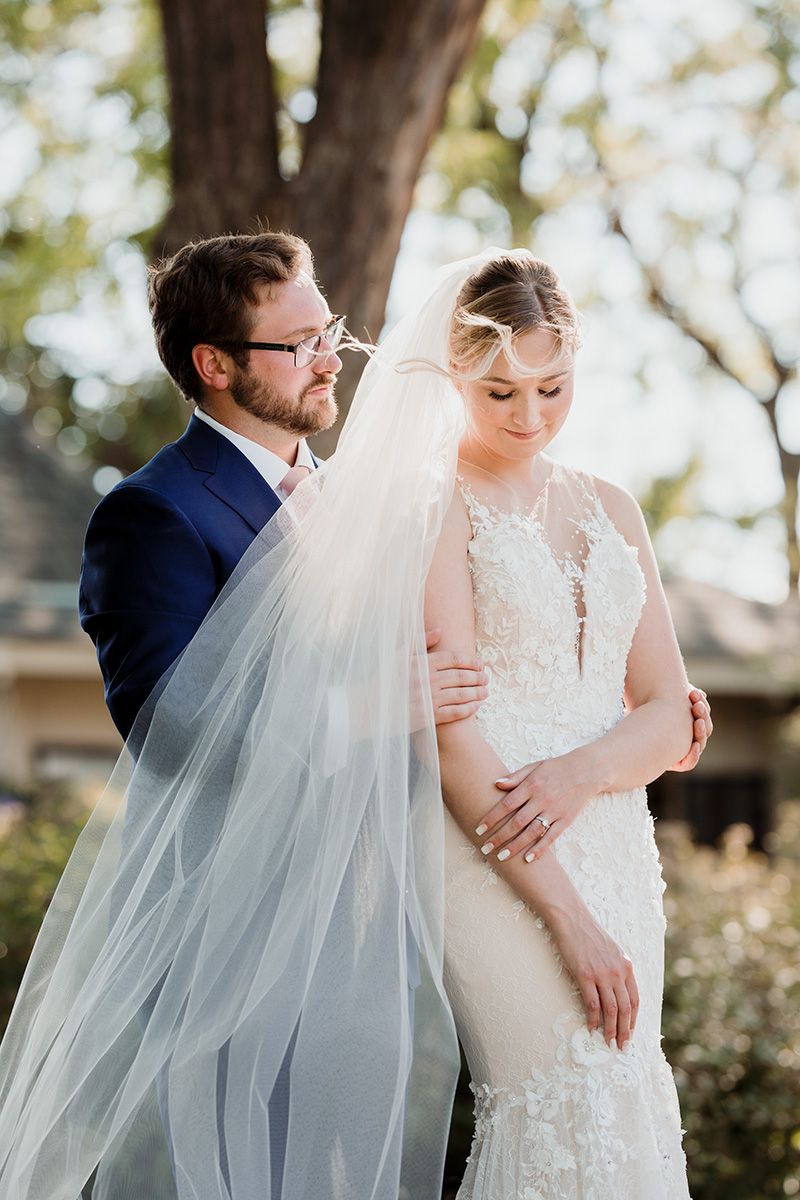 A romantic wedding couple shares an  intimate moment in an outdoor setting with soft natural lighting and a flowing veil.