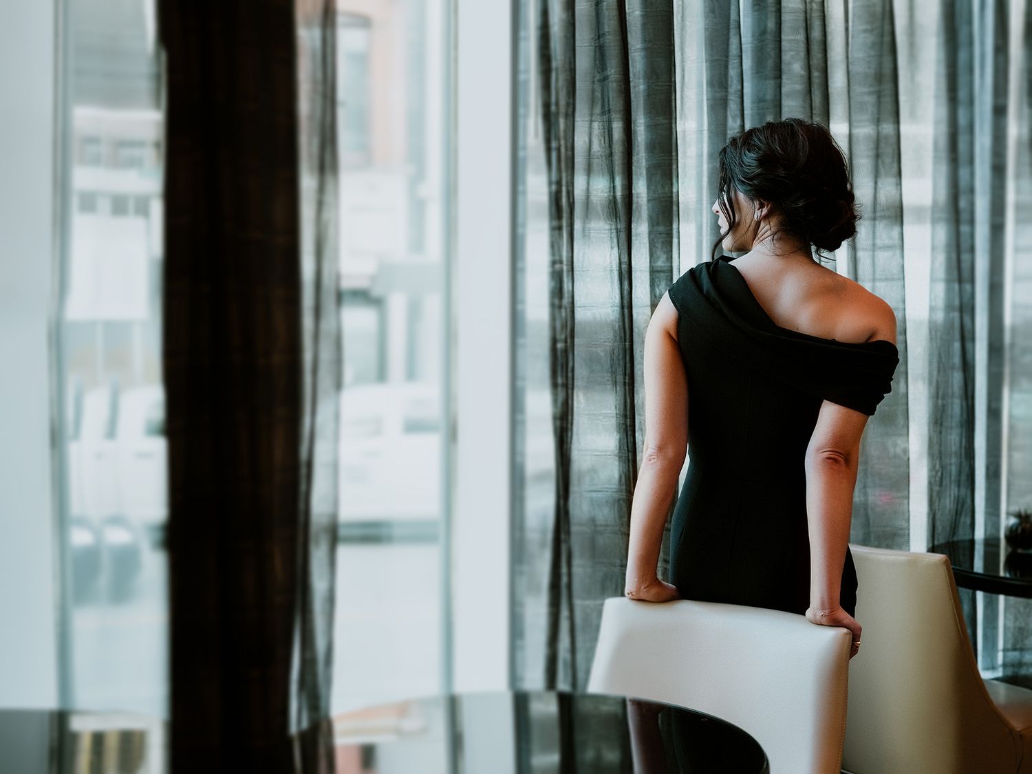 A woman in a black top stands in a modern office hallway with glass walls and reflective surfaces.