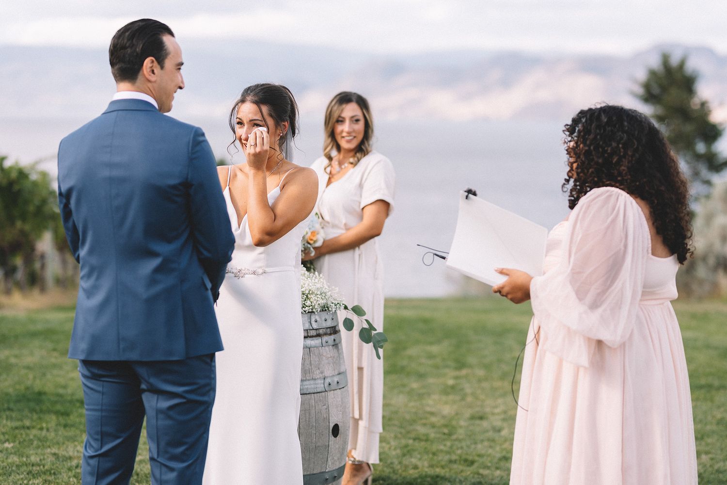 Elegant outdoor wedding ceremony with people in formal attire gathered in a sunlit field.