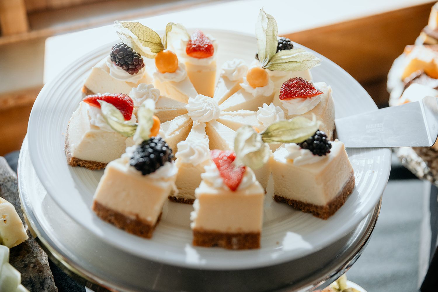 Small square cheesecake bites topped with fresh fruit and berries arranged on white plates.