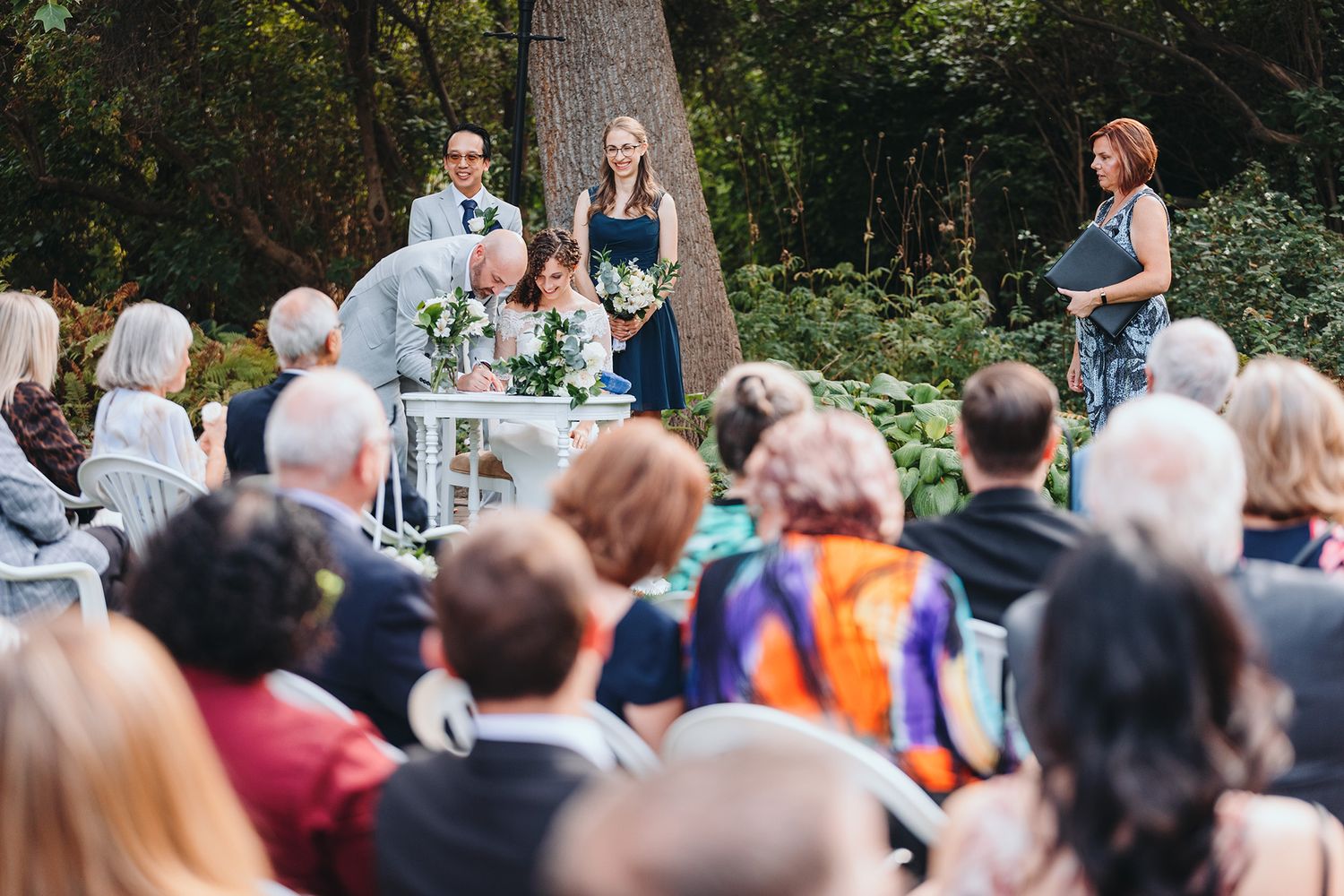 Wedding guests gathered outdoors at the Guisichan House with trees and foliage visible in the background.