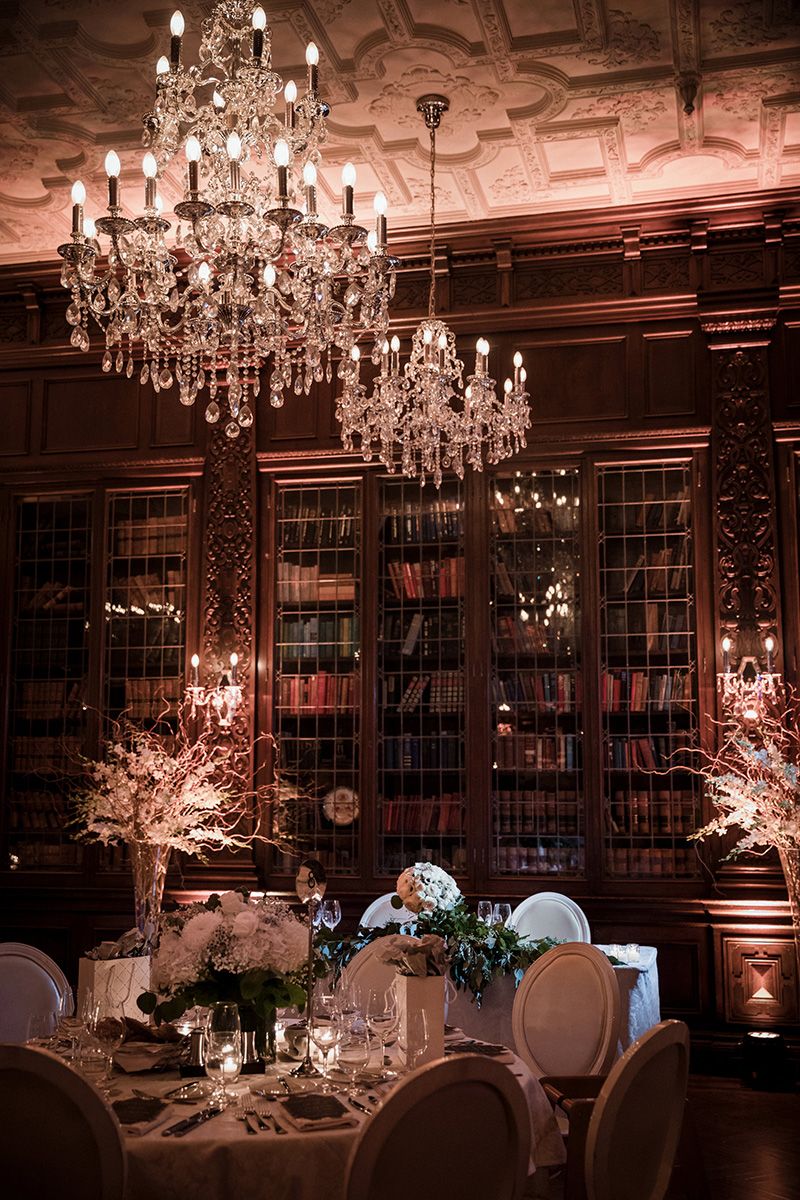 Elegant wedding reception venue with crystal chandeliers, white floral centrepieces, and romantic mood lighting.