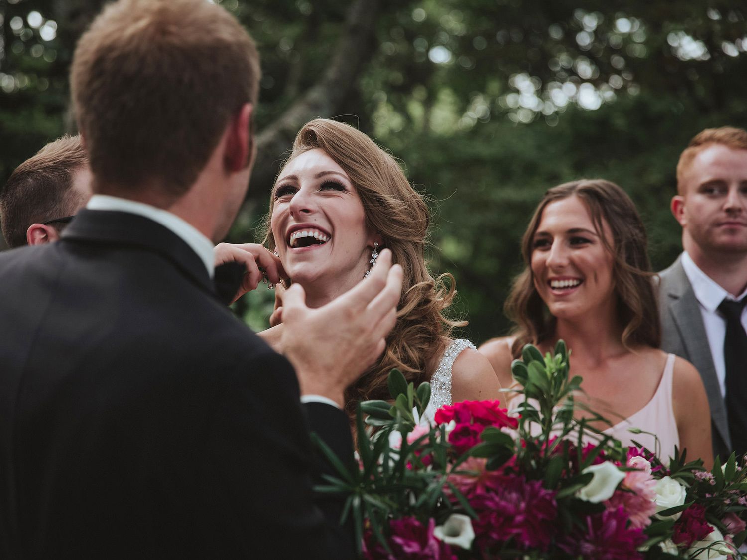 Wedding party members share joyful laughter during an outdoor celebration in a garden setting.
