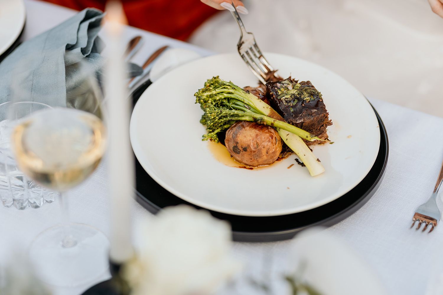 A collection of elegant plated dishes and wine glasses arranged on a white tablecloth in a fine dining setting.