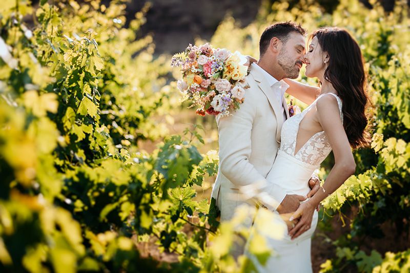 A romantic couple shares tender moments in a sun-drenched vineyard with golden light filtering through grape vines.