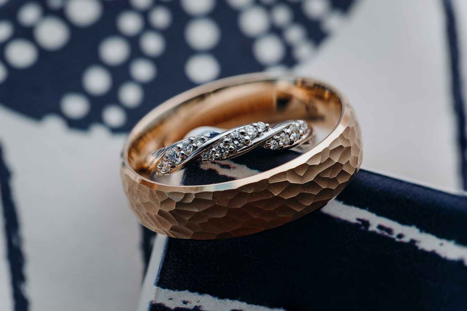 Two gold wedding rings with intricate carved patterns displayed on a dark background with bokeh lights.