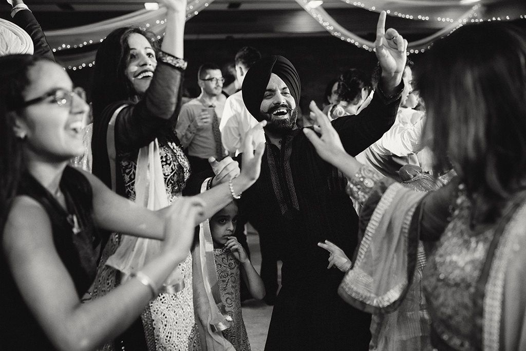 A black and white photo showing people dancing and celebrating at a Sikh wedding reception.