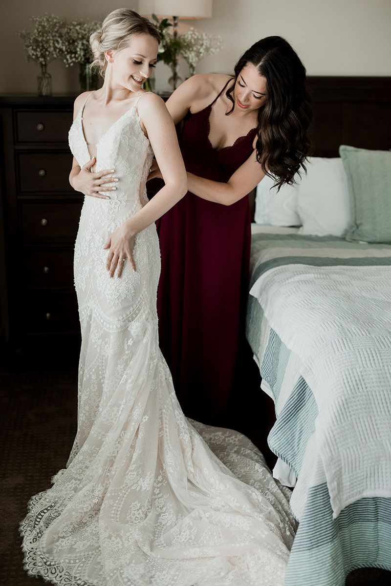 Two people in a bedroom share an intimate moment while one wears a stunning lace wedding dress with delicate details.