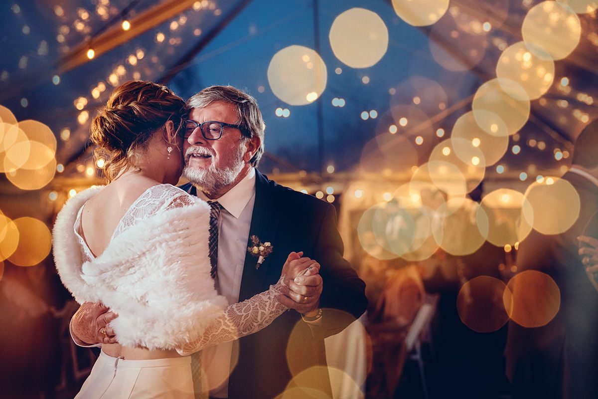 A bride and her father share a special dance under twinkling lights at a wedding reception, creating a magical atmosphere.