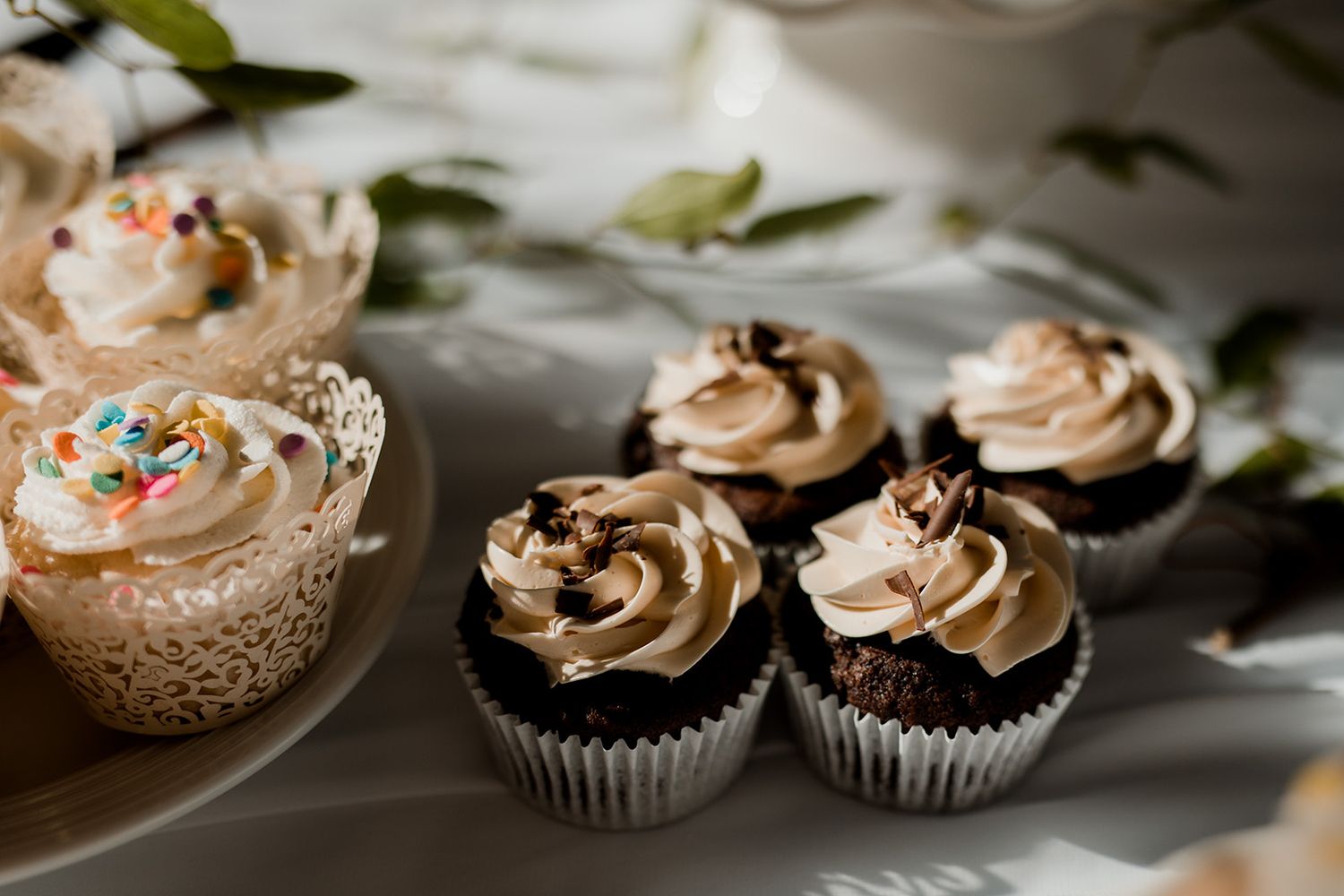 Chocolate cupcakes with swirled mocha frosting arranged on rustic plates with scattered green leaves for decoration.
