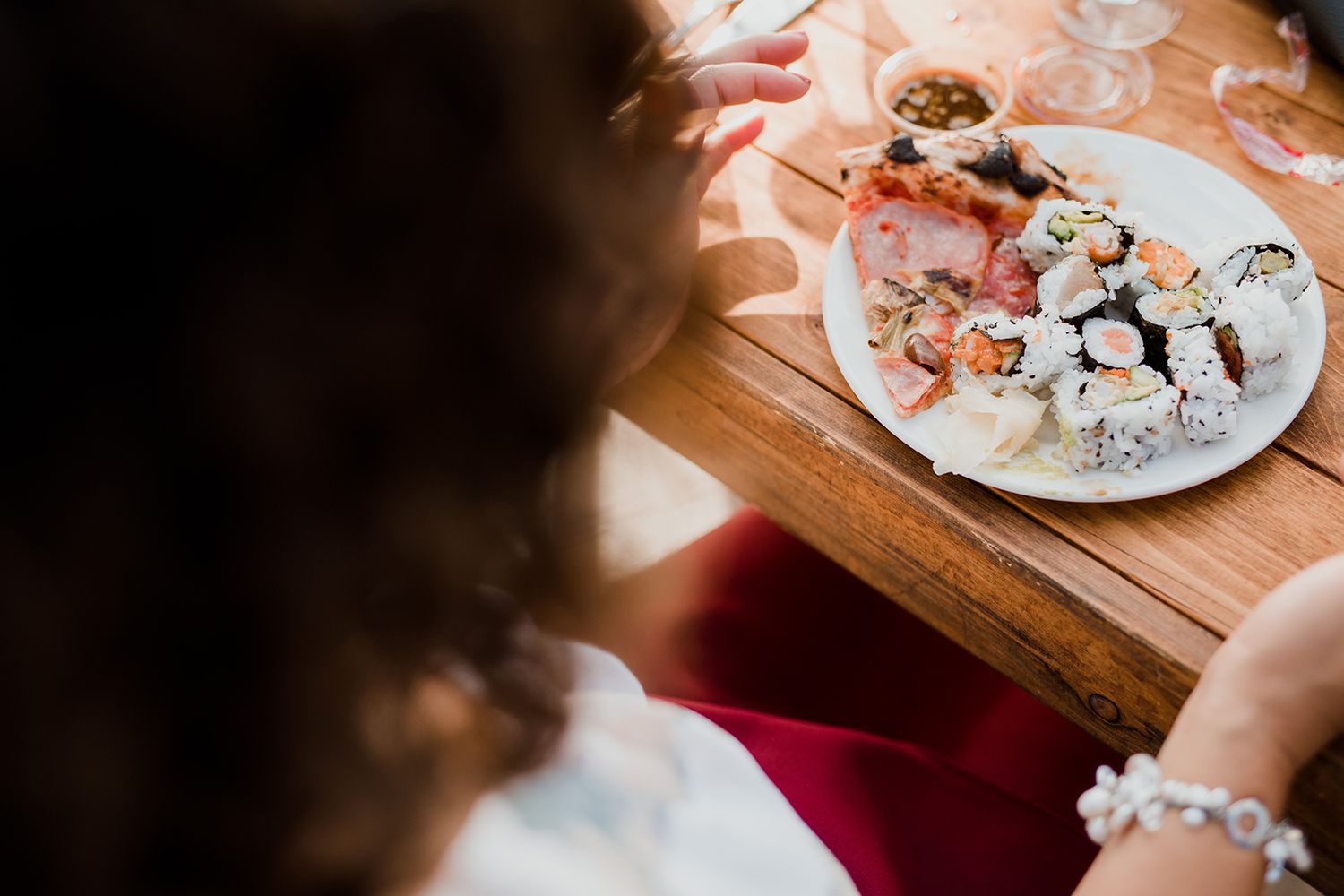 Person enjoying assorted sushi rolls and maki on wooden serving board at restaurant table.