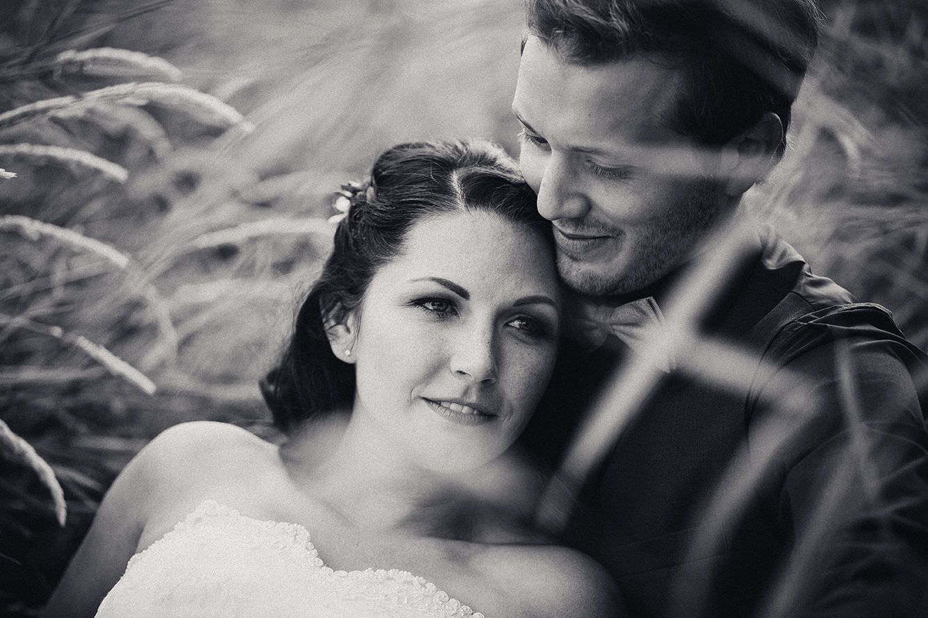 Black and white romantic wedding portrait of a couple embracing while sitting among tall grass.