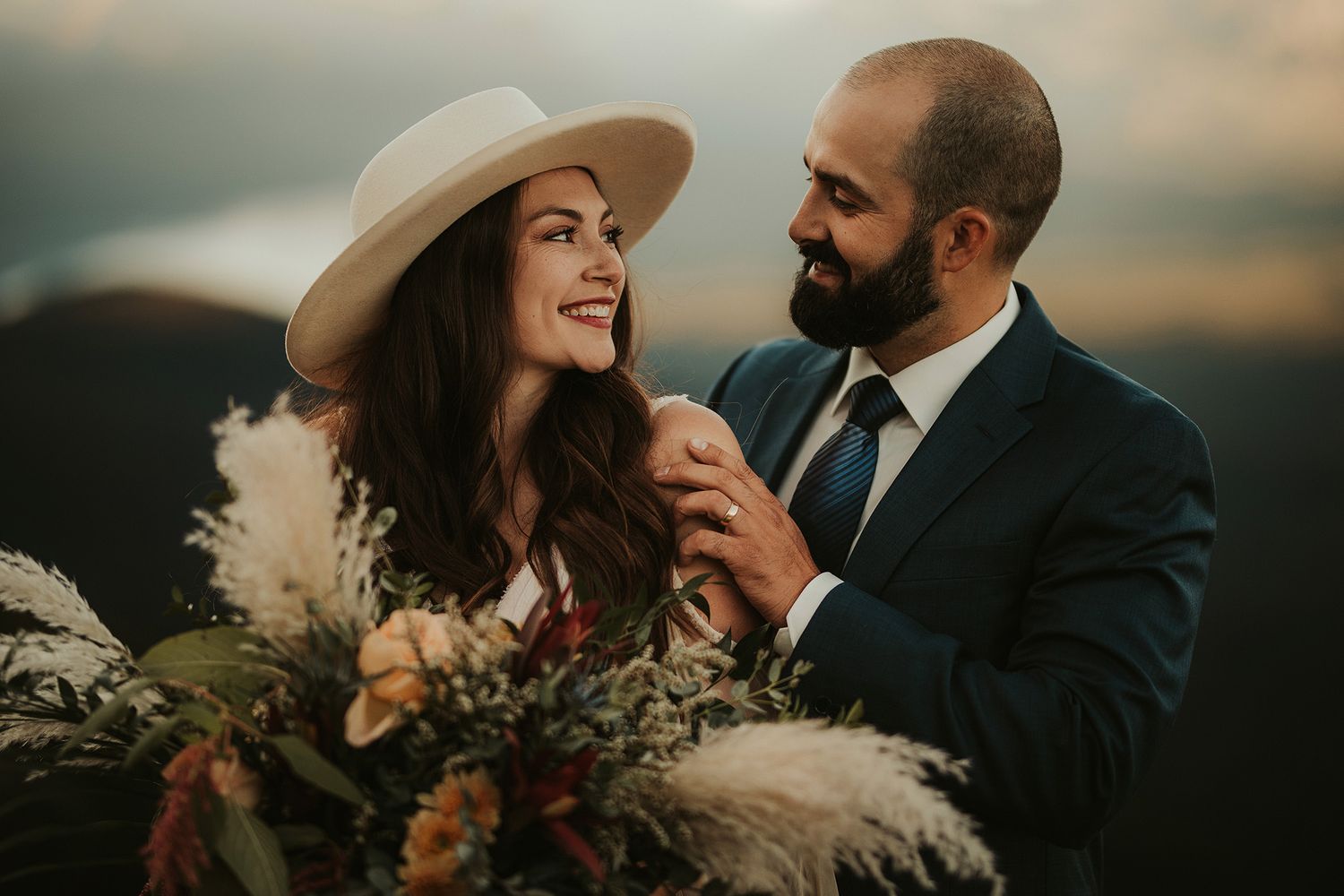 A couple shares an intimate moment at sunset with a bouquet of wildflowers in a romantic outdoor setting.