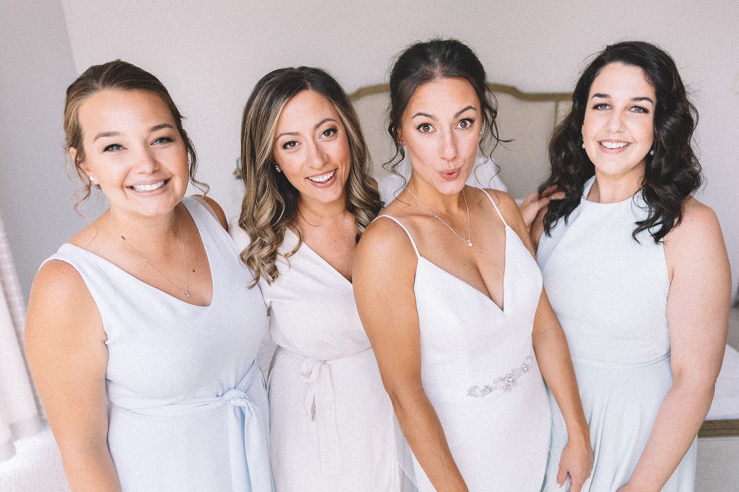 Group photo of bridesmaids wearing matching pastel dresses while getting ready for a wedding celebration.