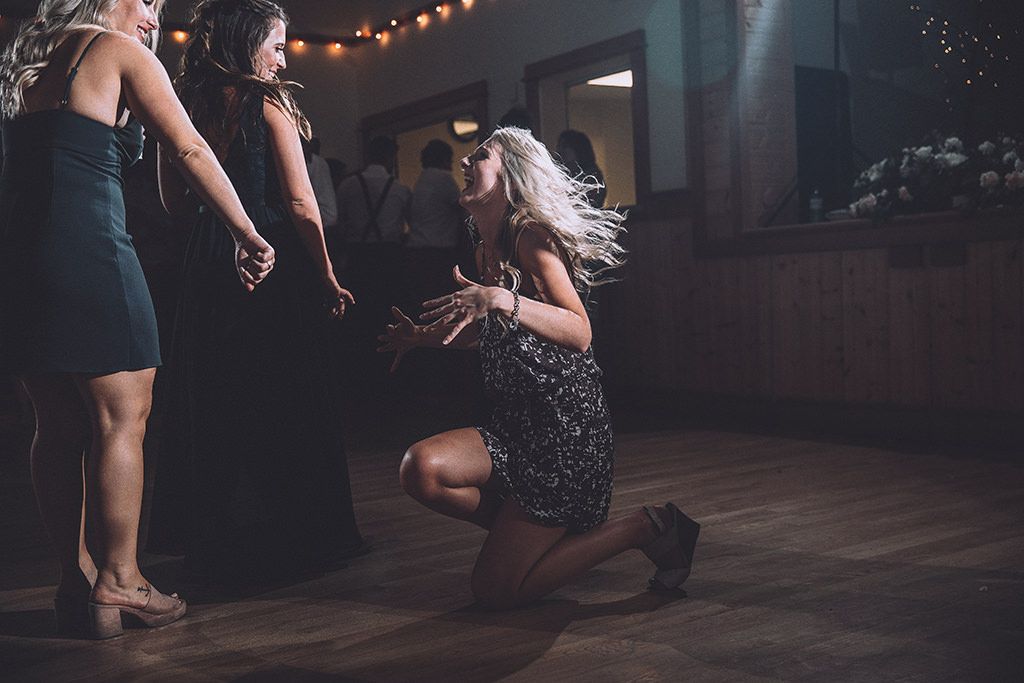 Two people dance together in an intimate pose under warm string lights at a dimly lit indoor venue.
