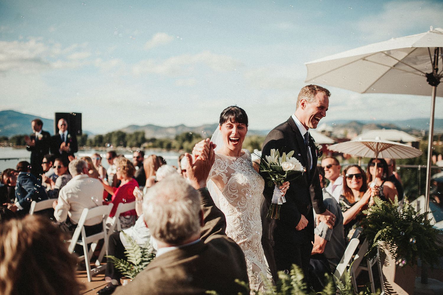 A Hotel Eldorado roof-top wedding celebration showing guests cheering a bride and groom under white umbrellas on a sunny day.