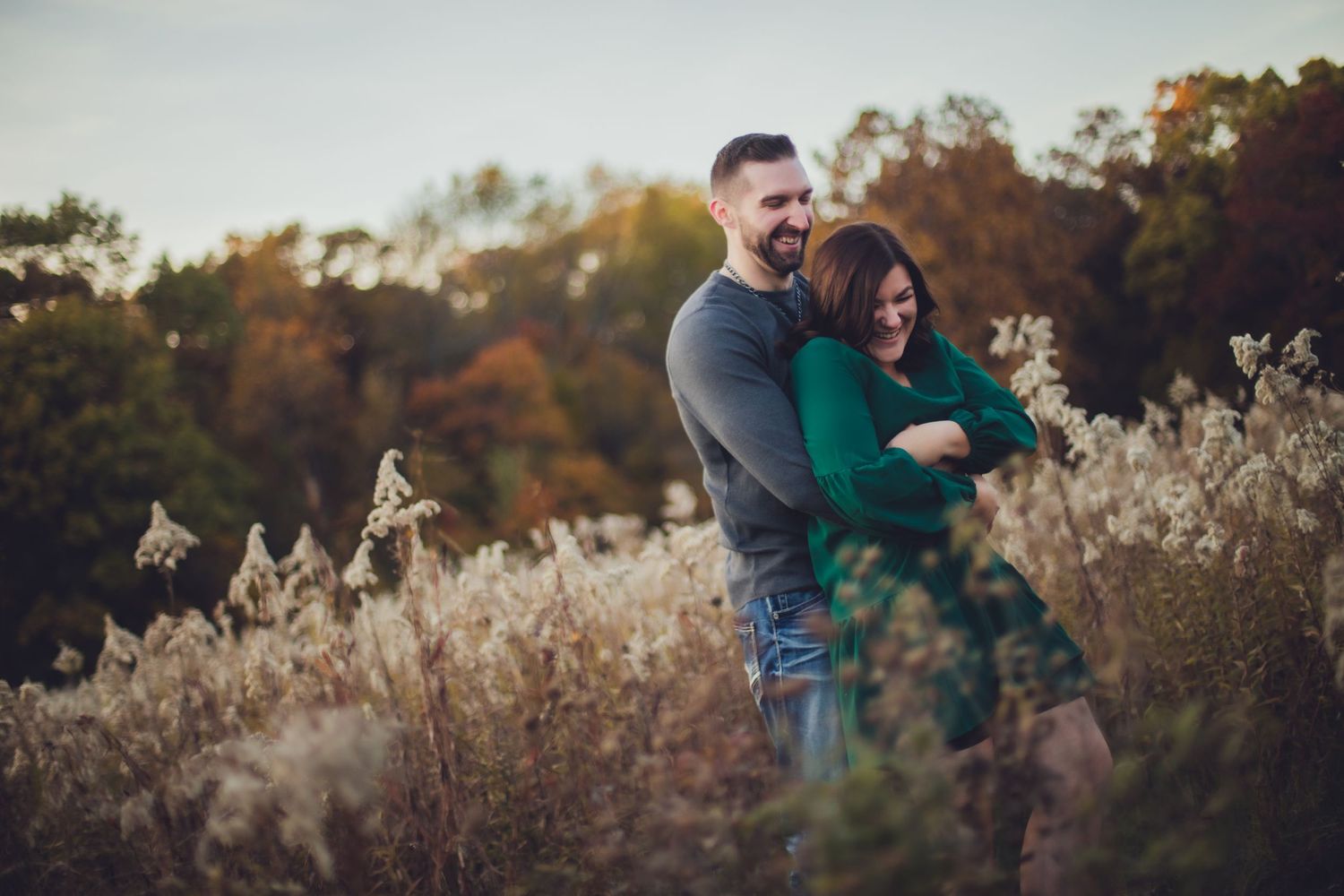 Couple laughing together during their fall engagement photo session in a meadow.