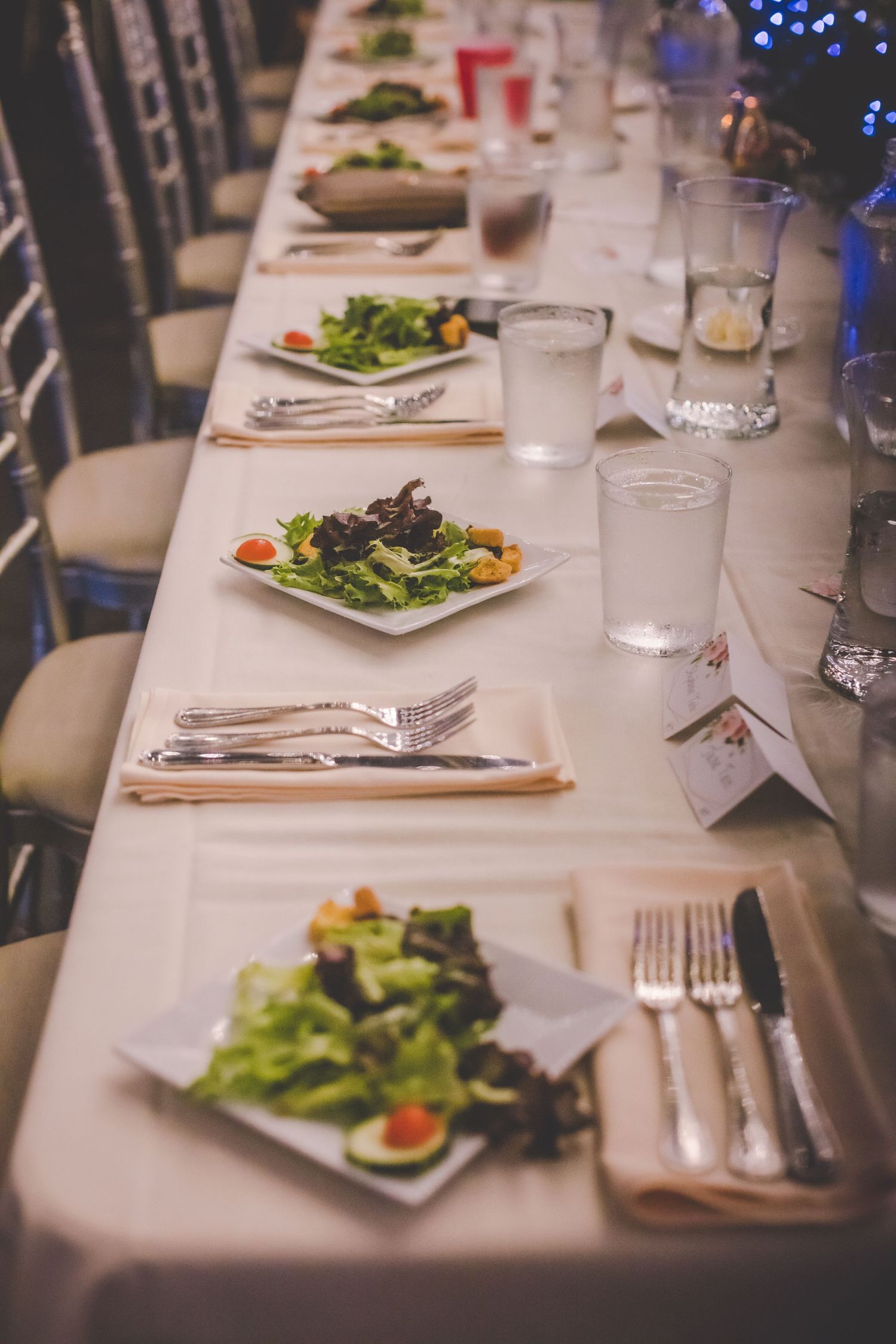 Elegant wedding reception table setting with white linens, salad plates, and formal place settings.