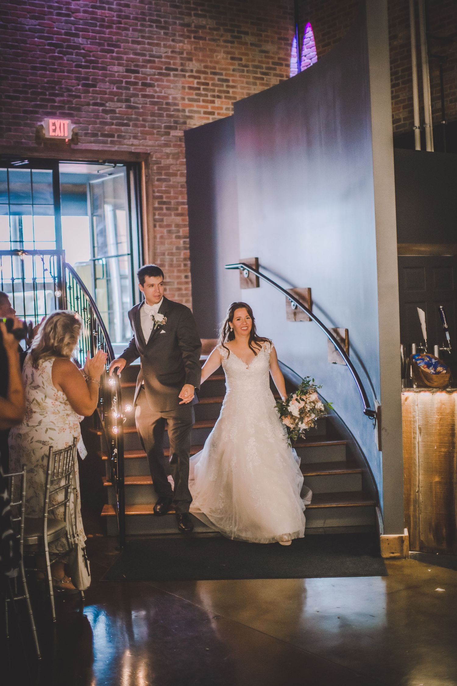 Wedding reception entrance sequence showing couple descending stairs in industrial-chic venue.