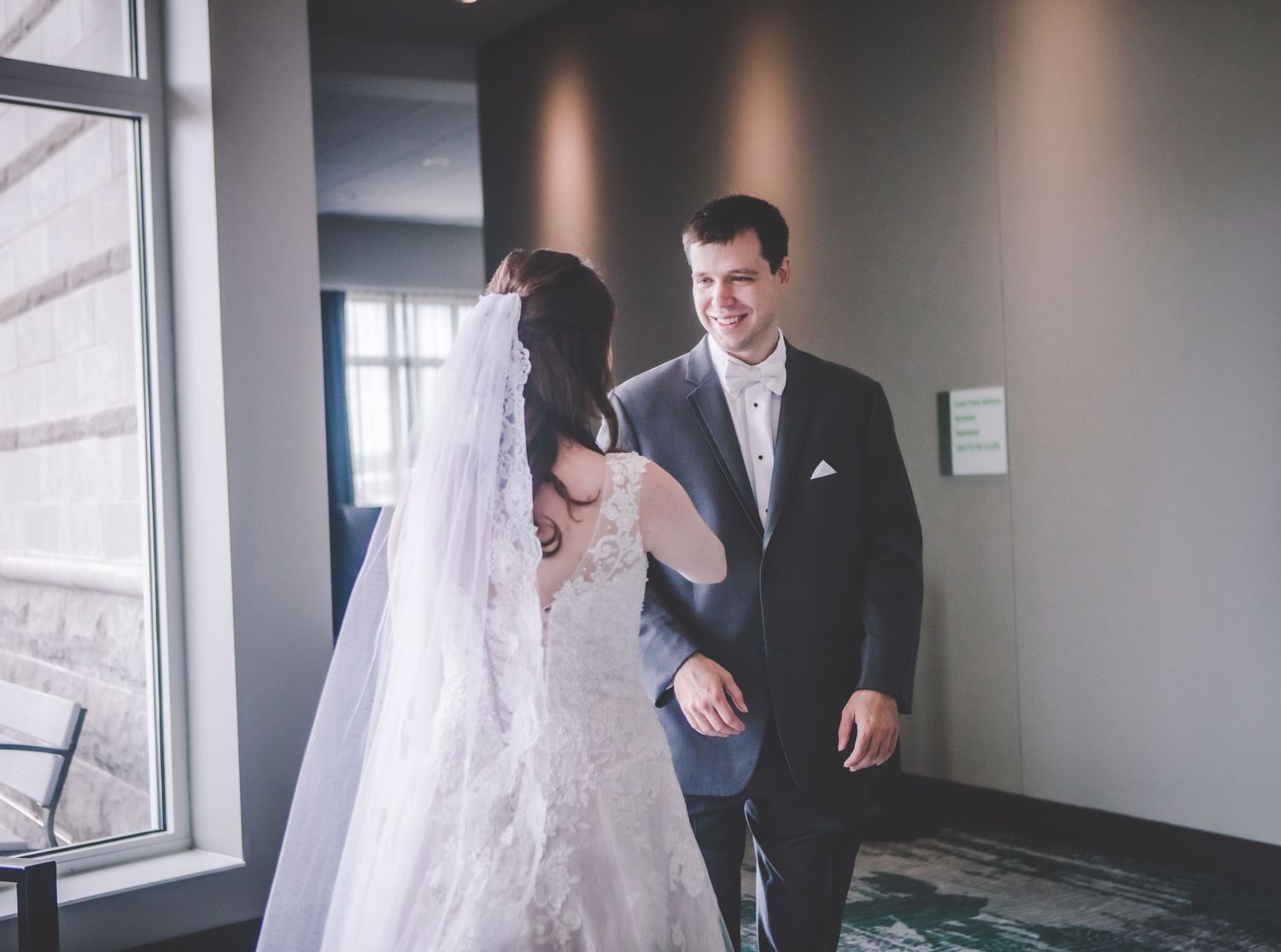 A couple shares an intimate moment during their wedding first look in a modern venue hallway.