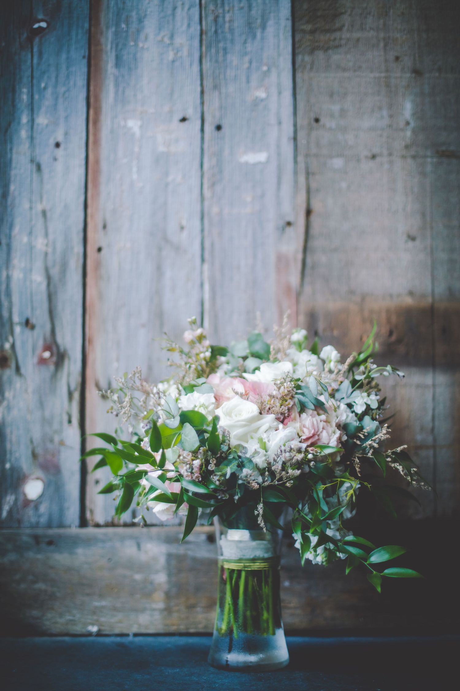 Rustic floral arrangements in glass vases against weathered blue wooden wall.