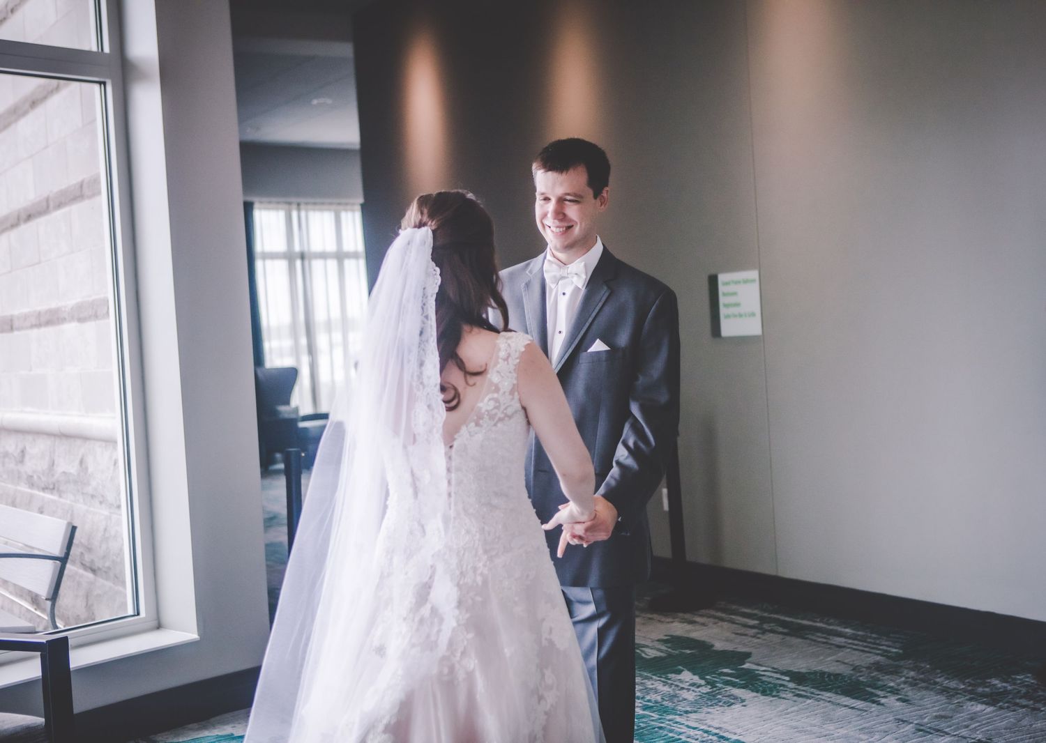A sweet exchange between newlyweds standing in front of large windows.