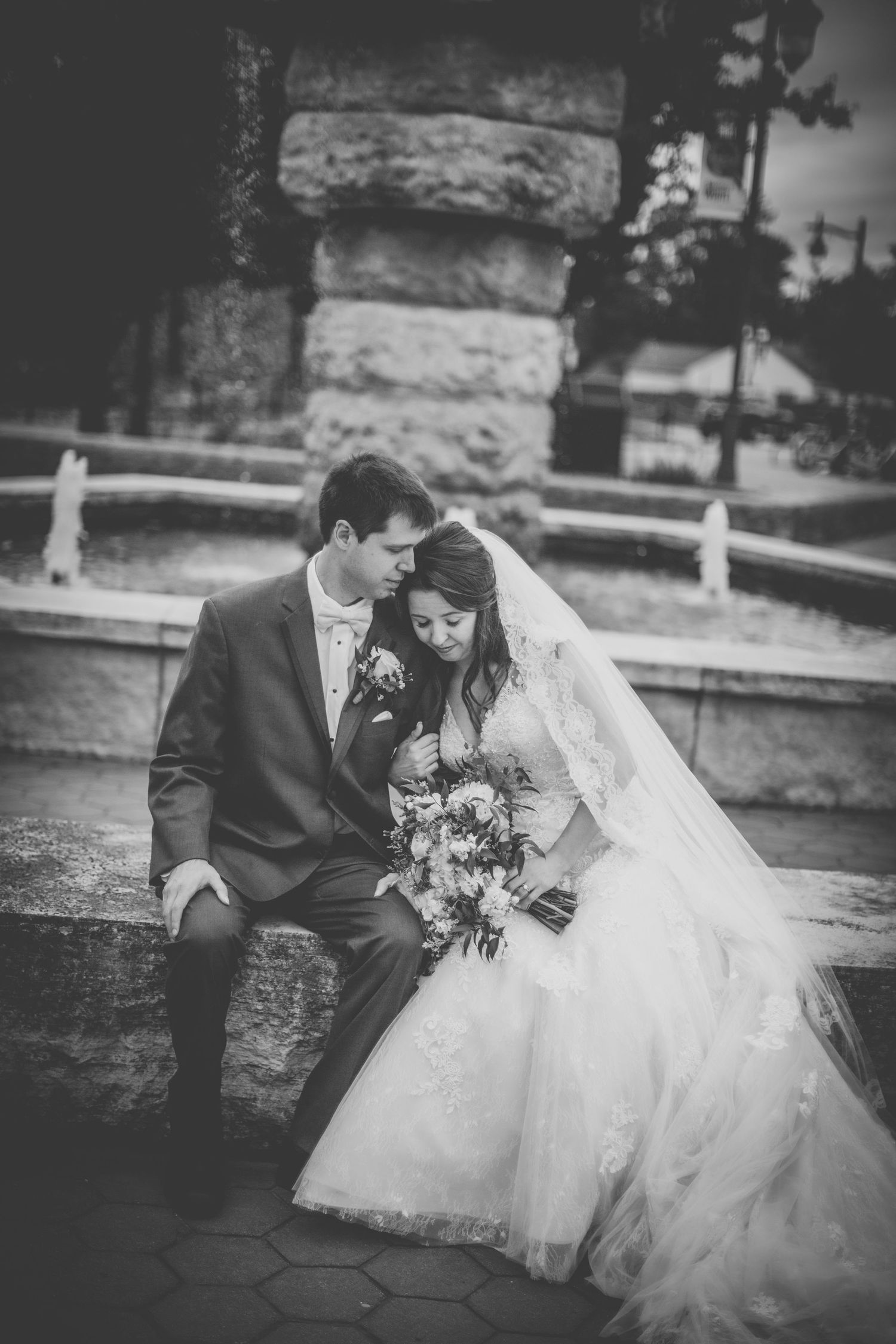Black and white portrait of wedding couple seated intimately on stone steps.