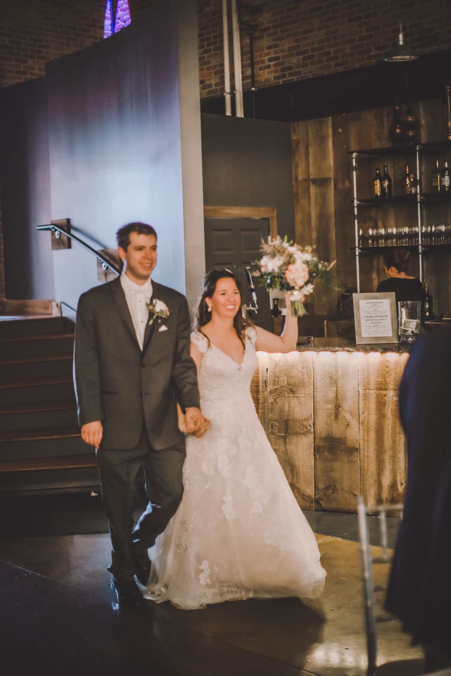 Newlyweds make their way through rustic reception venue with exposed brick and mood lighting.