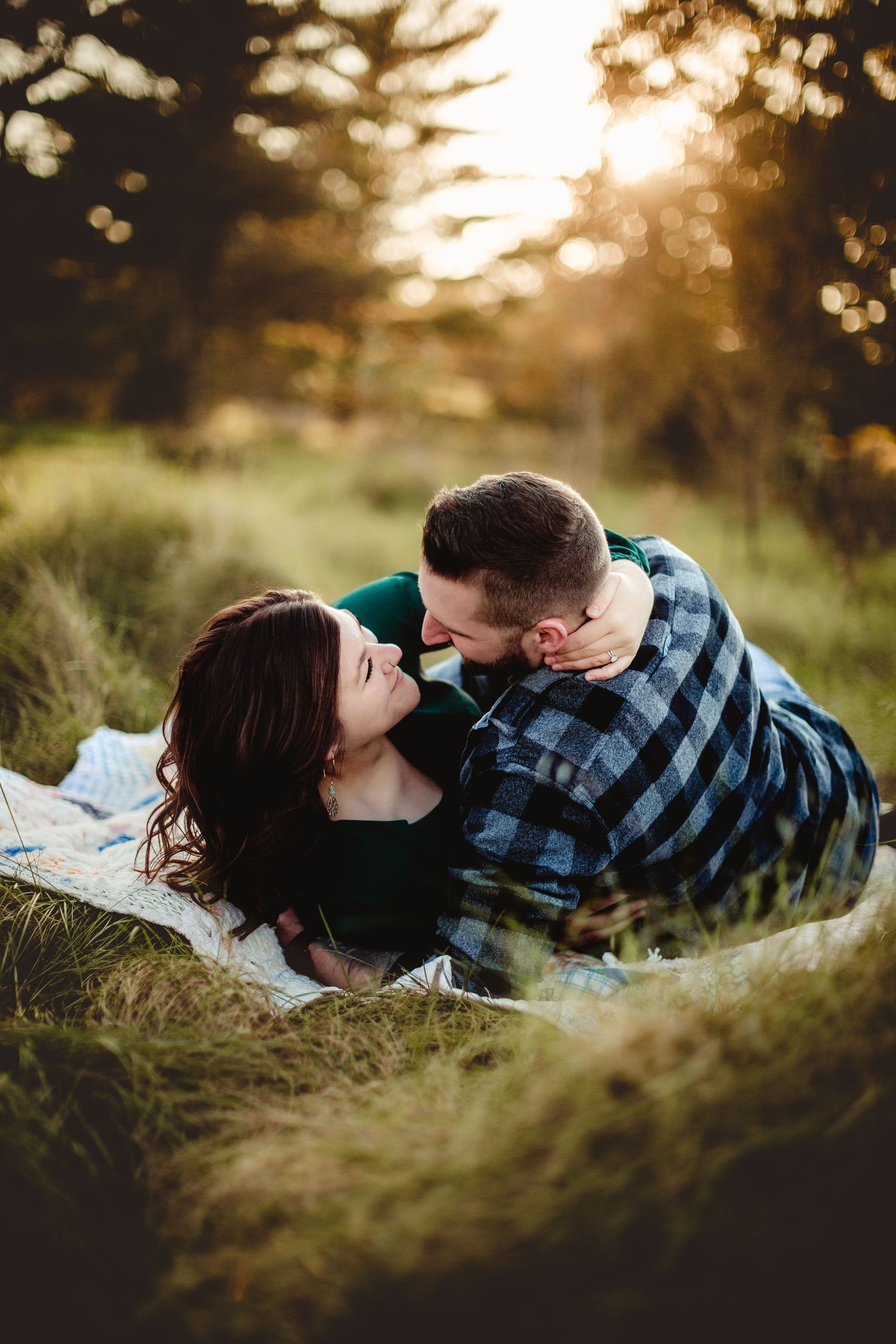 Romantic couple lying in tall grass during sunset with bokeh lighting.