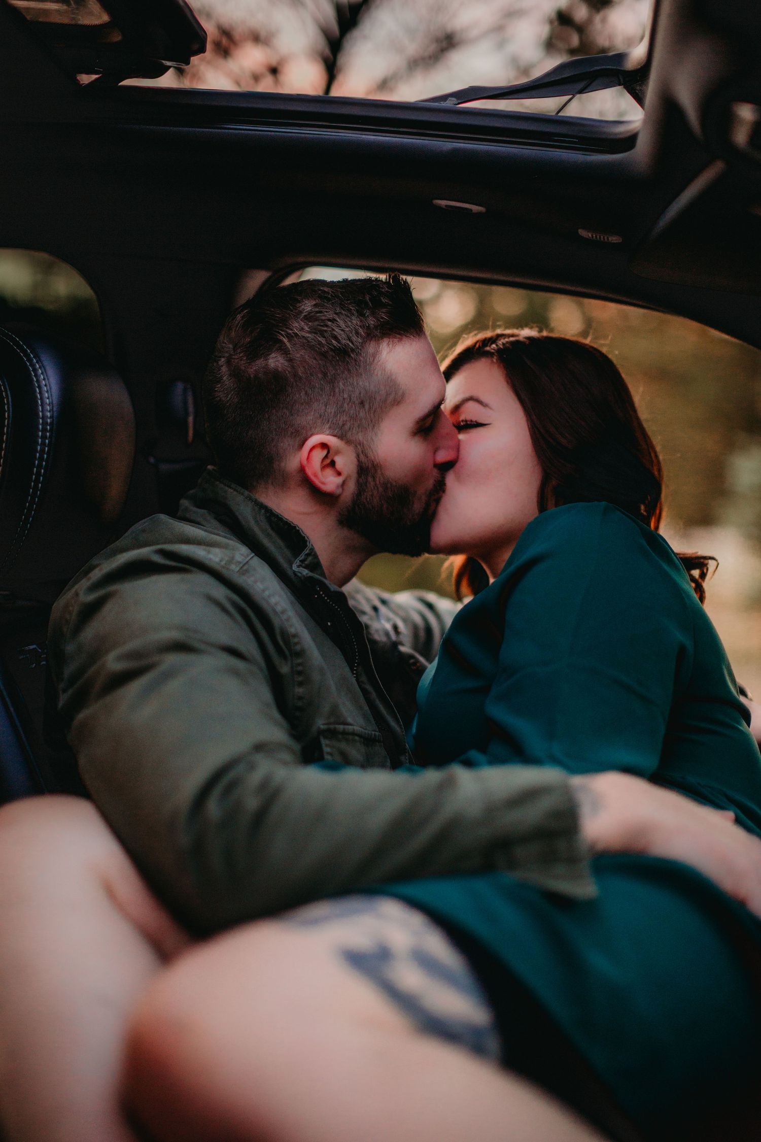 Passionate embrace photographed from interior car angle during sunset.