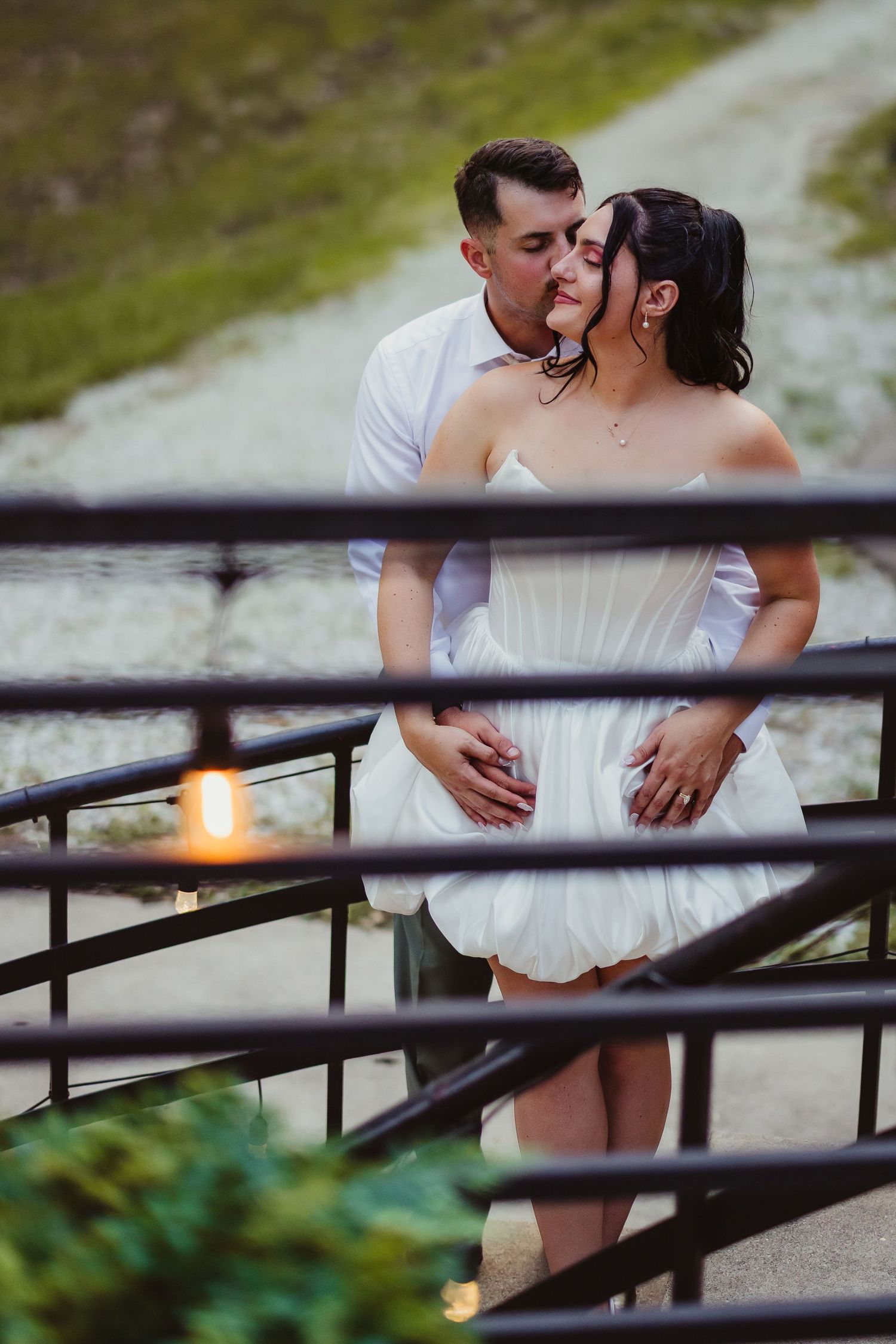 Romantic couple in white attire sharing a tender kiss on outdoor stairs with candlelight ambiance.