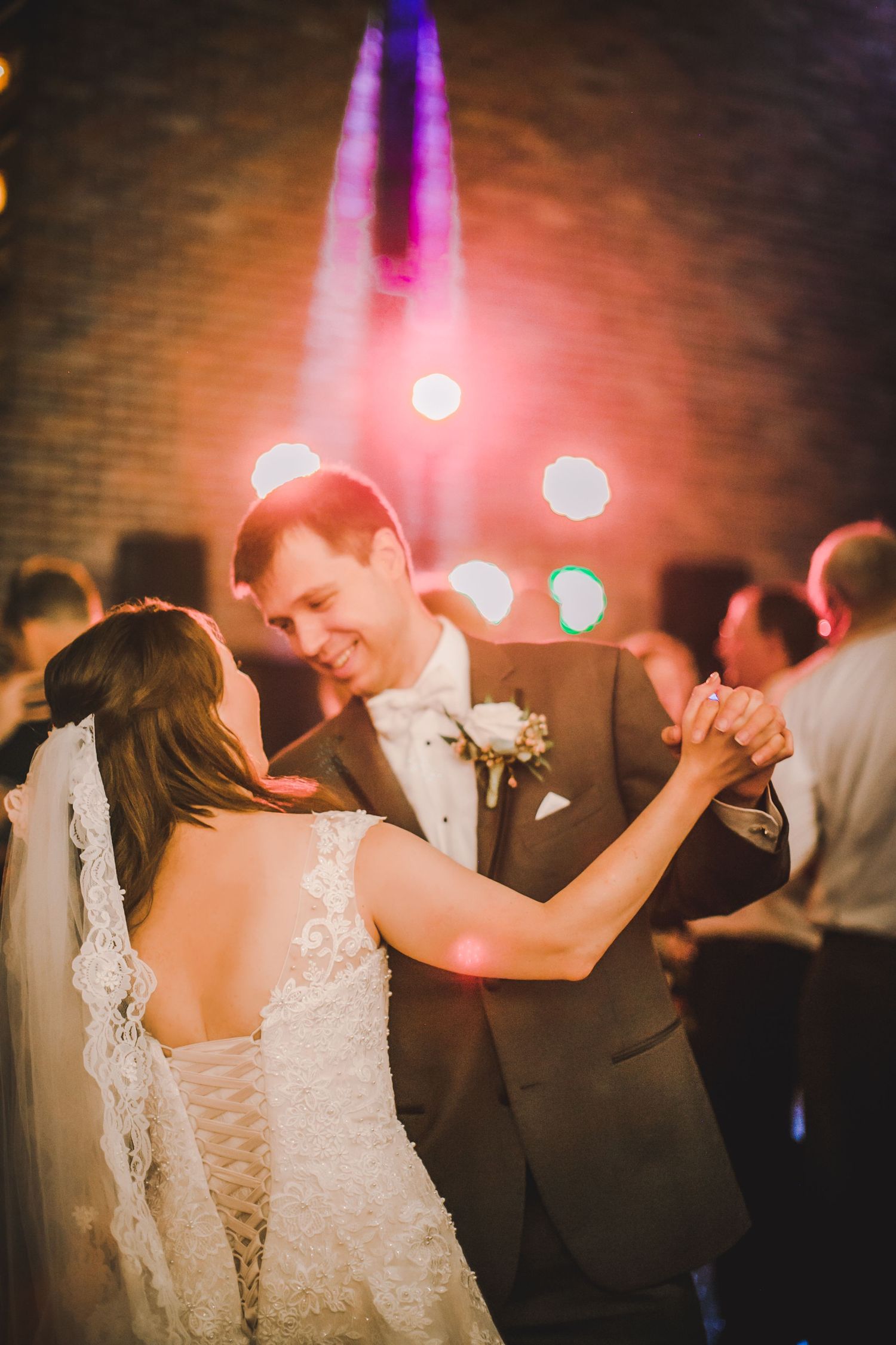Newlyweds dance together under warm lighting at their wedding reception with vintage-style decor.