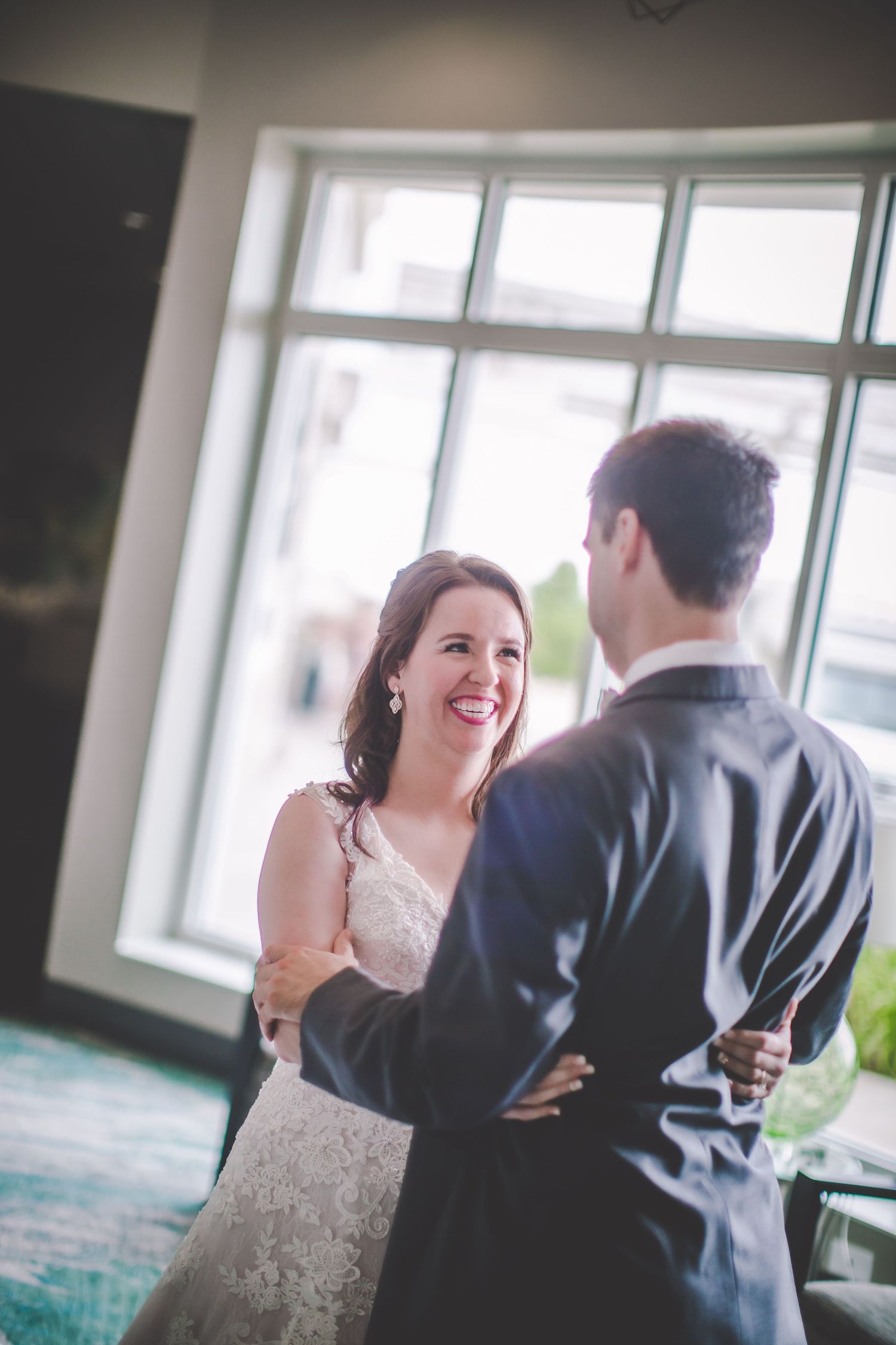 A joyful moment between a couple in formal attire near large windows.