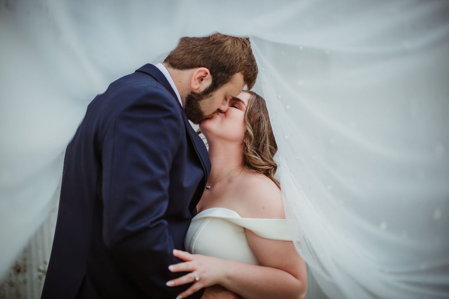 An intimate close-up of a tender wedding day kiss against a soft white background.