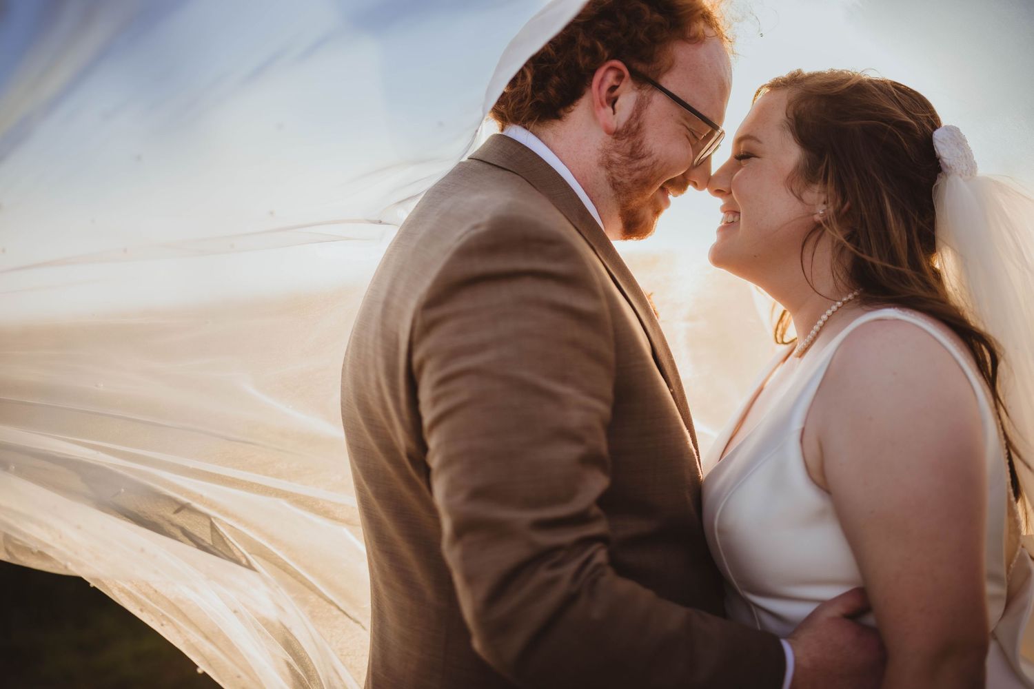 A romantic intimate wedding portrait captured against a bright outdoor backdrop with soft lighting.