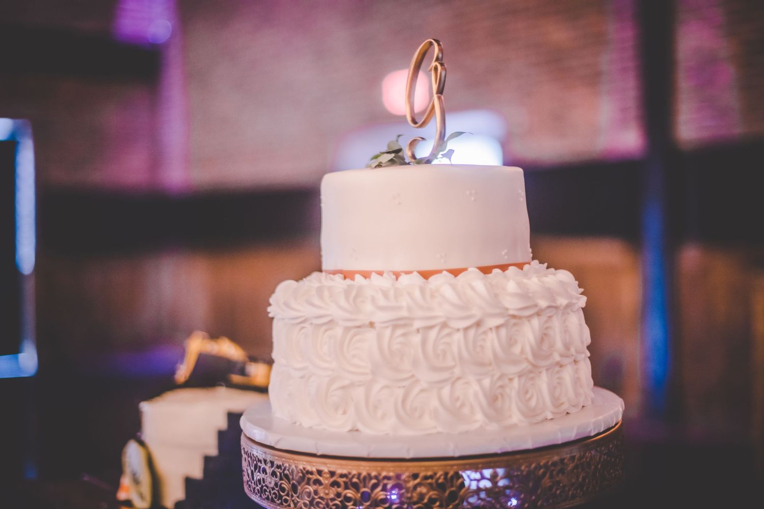 Elegant white wedding cake with ruffled tiers and a gold monogram topper on a metallic stand.