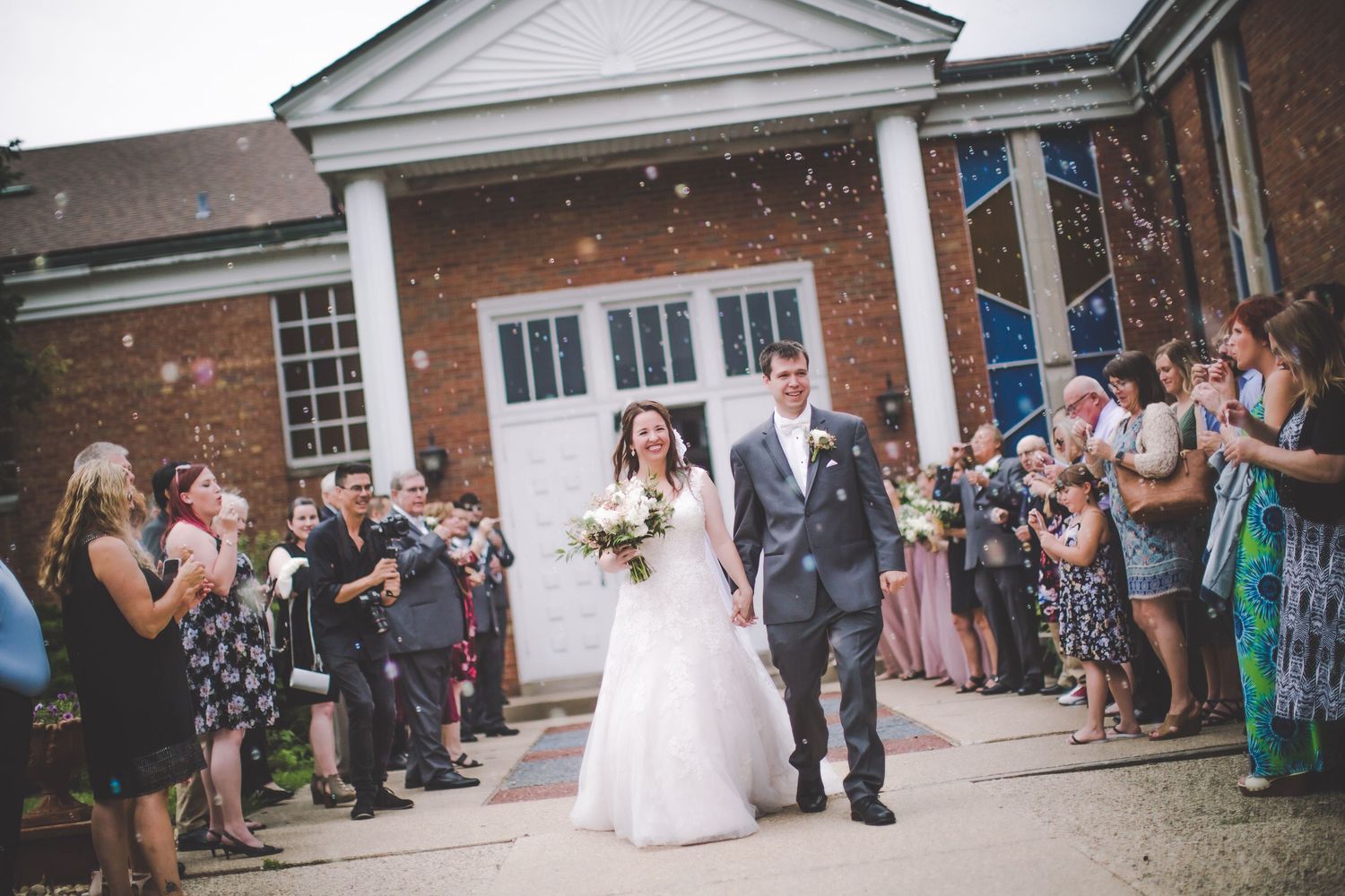 Celebratory wedding scene with crowd outside traditional brick church building.
