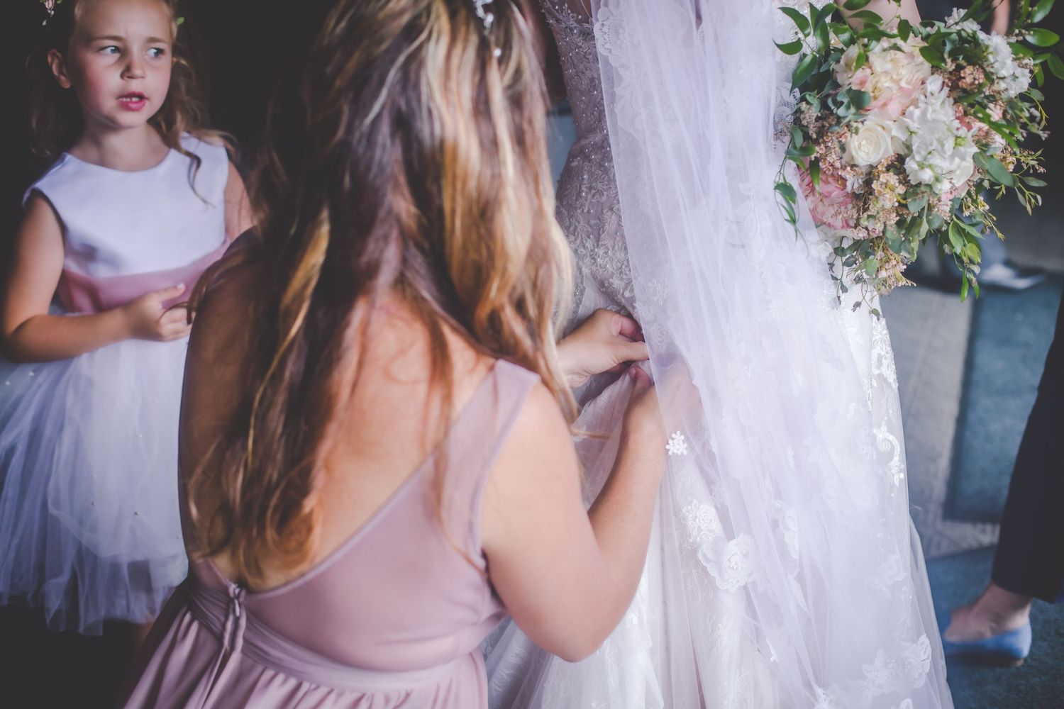 A bridesmaid in pink helps with final wedding dress preparations.